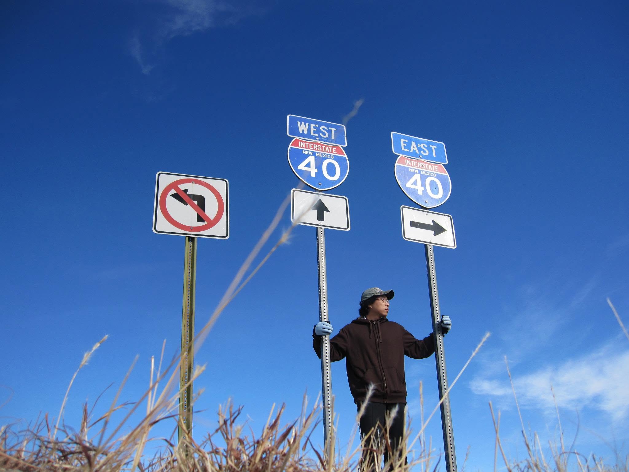 Standing between Interstate 40 East and West signs under a deep blue New Mexico sky