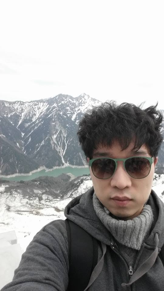 Selfie on the Tateyama Kurobe Alpine Route, snowy peaks and an emerald lake behind