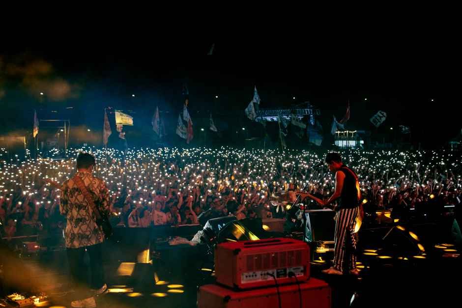 Two musicians on stage at night facing a crowd holding up phone lights at a Korean rock festival