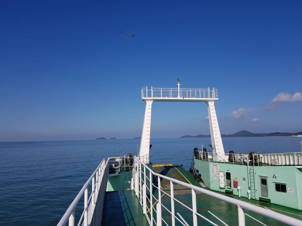 The open car deck of a Korean car ferry heading out to sea, islands on the horizon