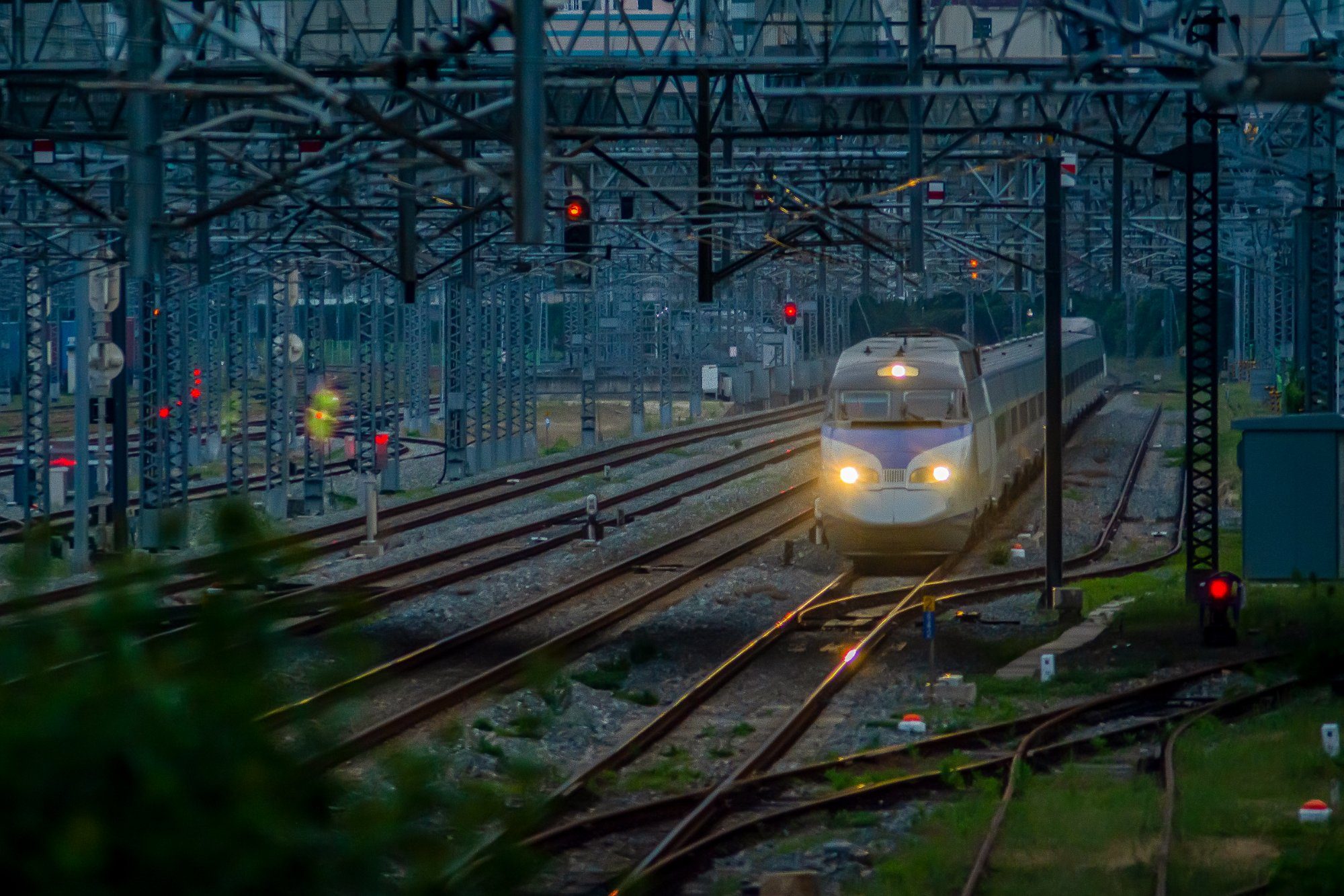 A KTX high-speed train pulling into a Seoul rail yard at dusk under overhead wires