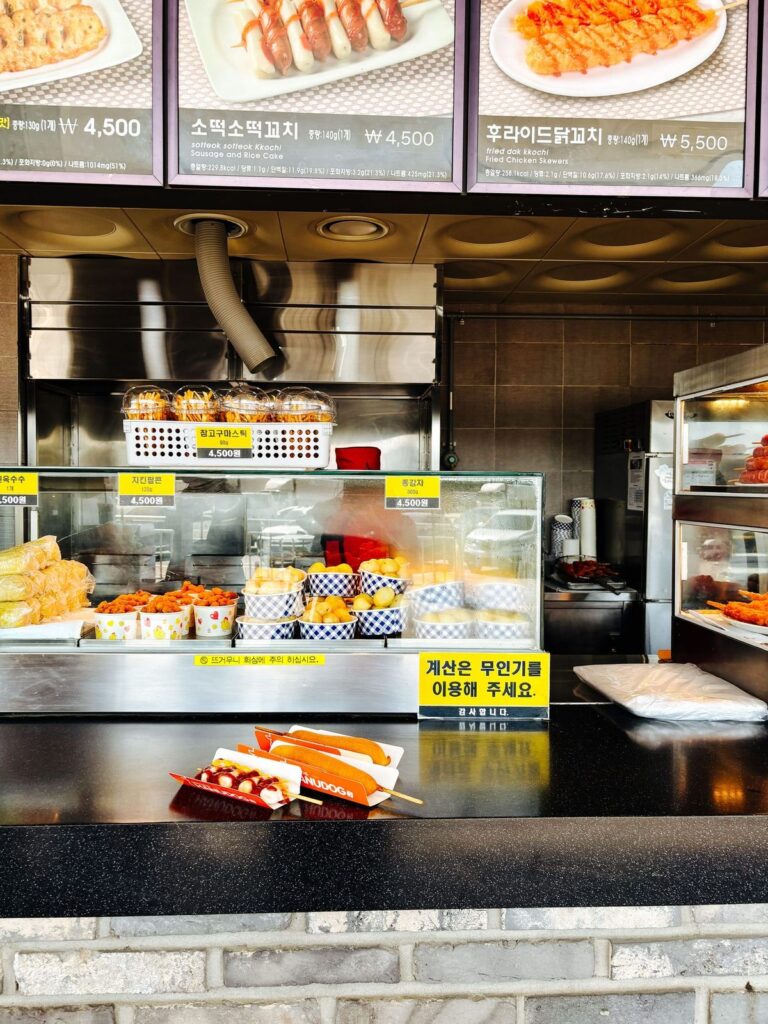 A motorway rest stop snack counter with corn dogs, skewers and baked potatoes