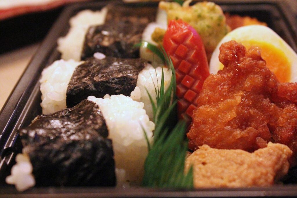 A dosirak lunch box with rice balls, fried chicken, sausage and egg