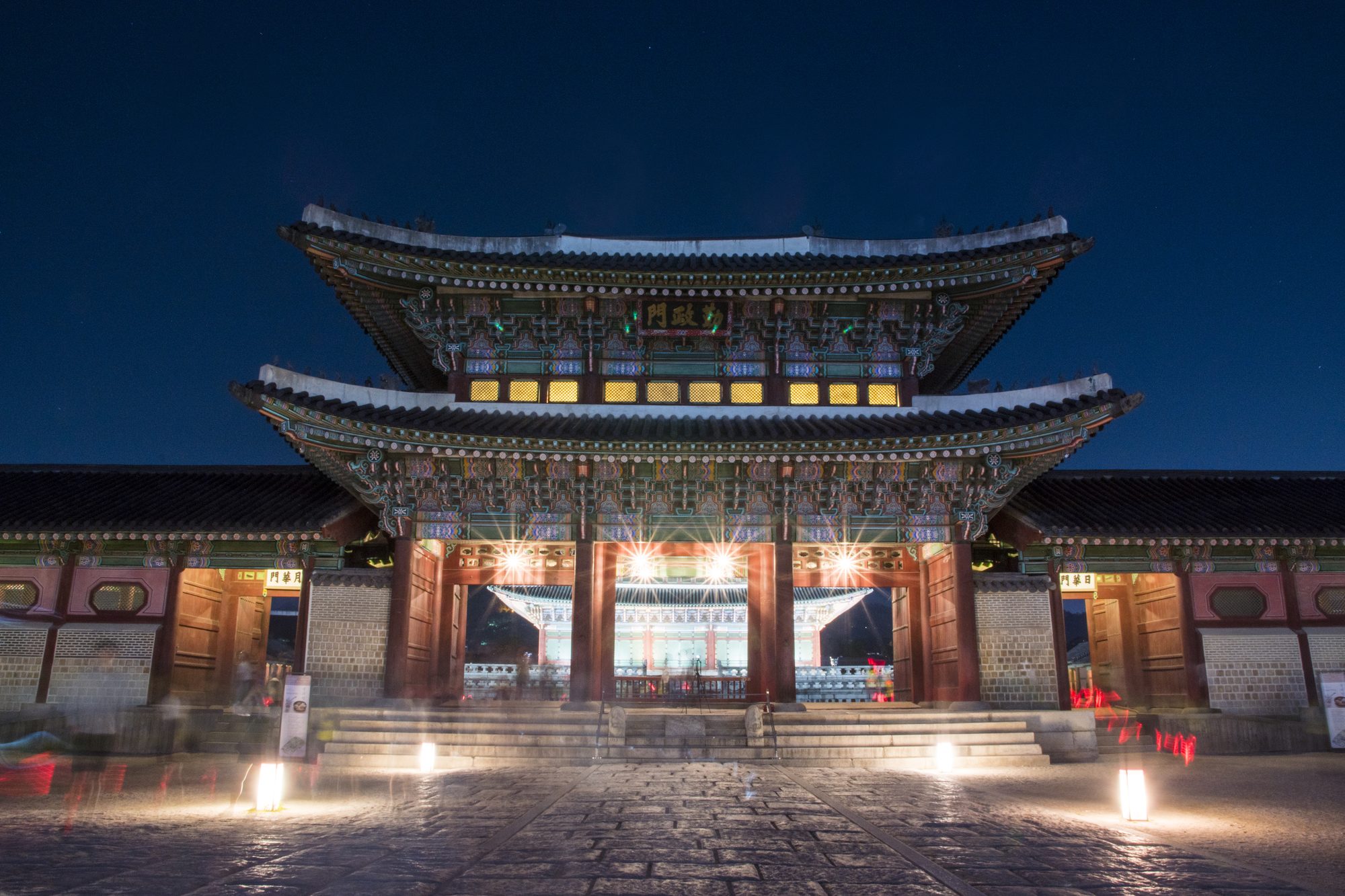 Geunjeongmun gate at Gyeongbokgung illuminated during the night viewing, with visitors walking through