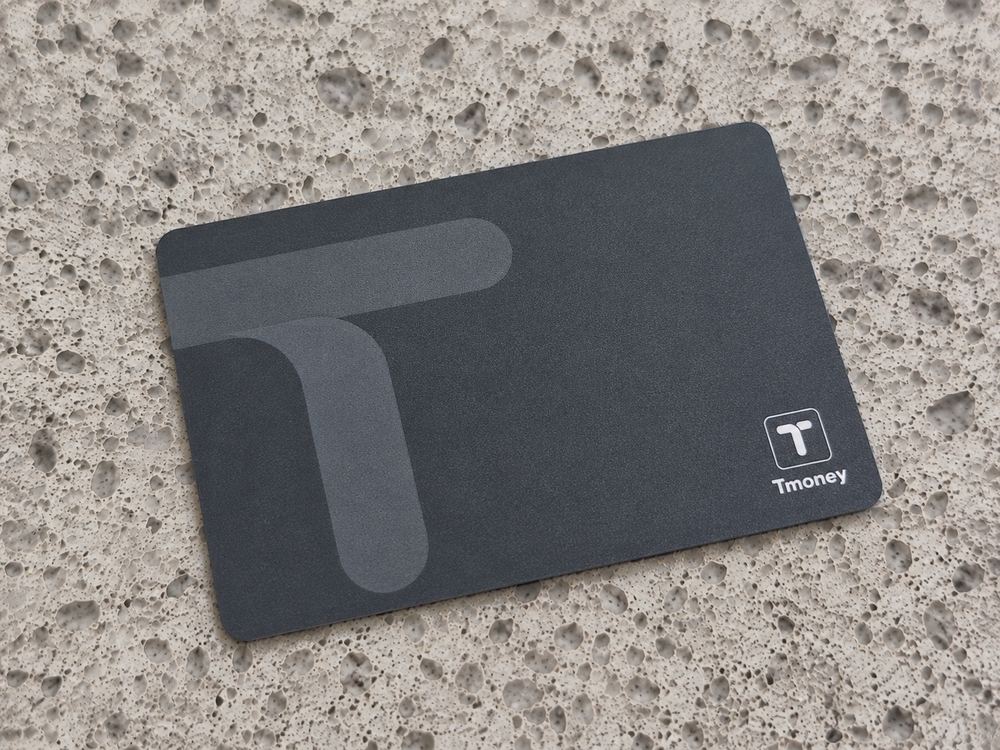 A plain charcoal T-money transit card on a stone surface