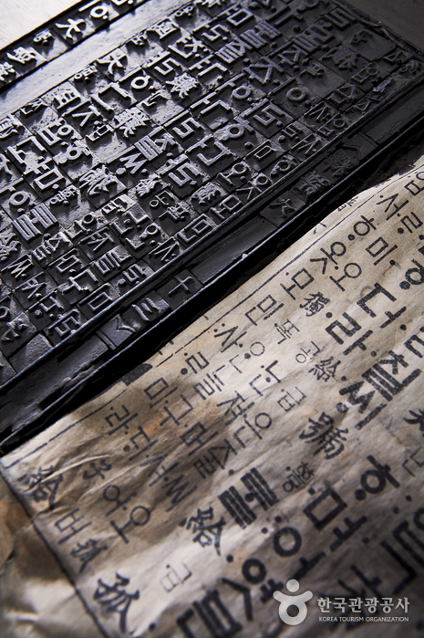 Close-up of old movable metal type for Hangeul letters, locked in a frame, beside a printed page of early Hangeul text.