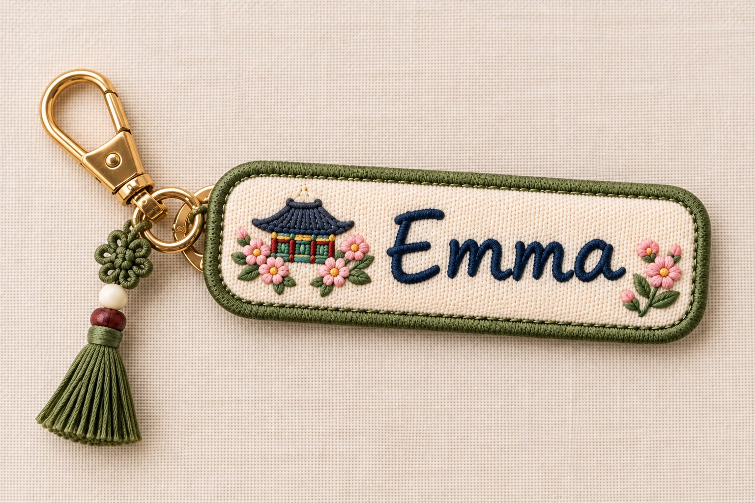 An illustration of an embroidered name tag on a brass clip with a green tassel and a small pavilion stitched beside the name Emma.