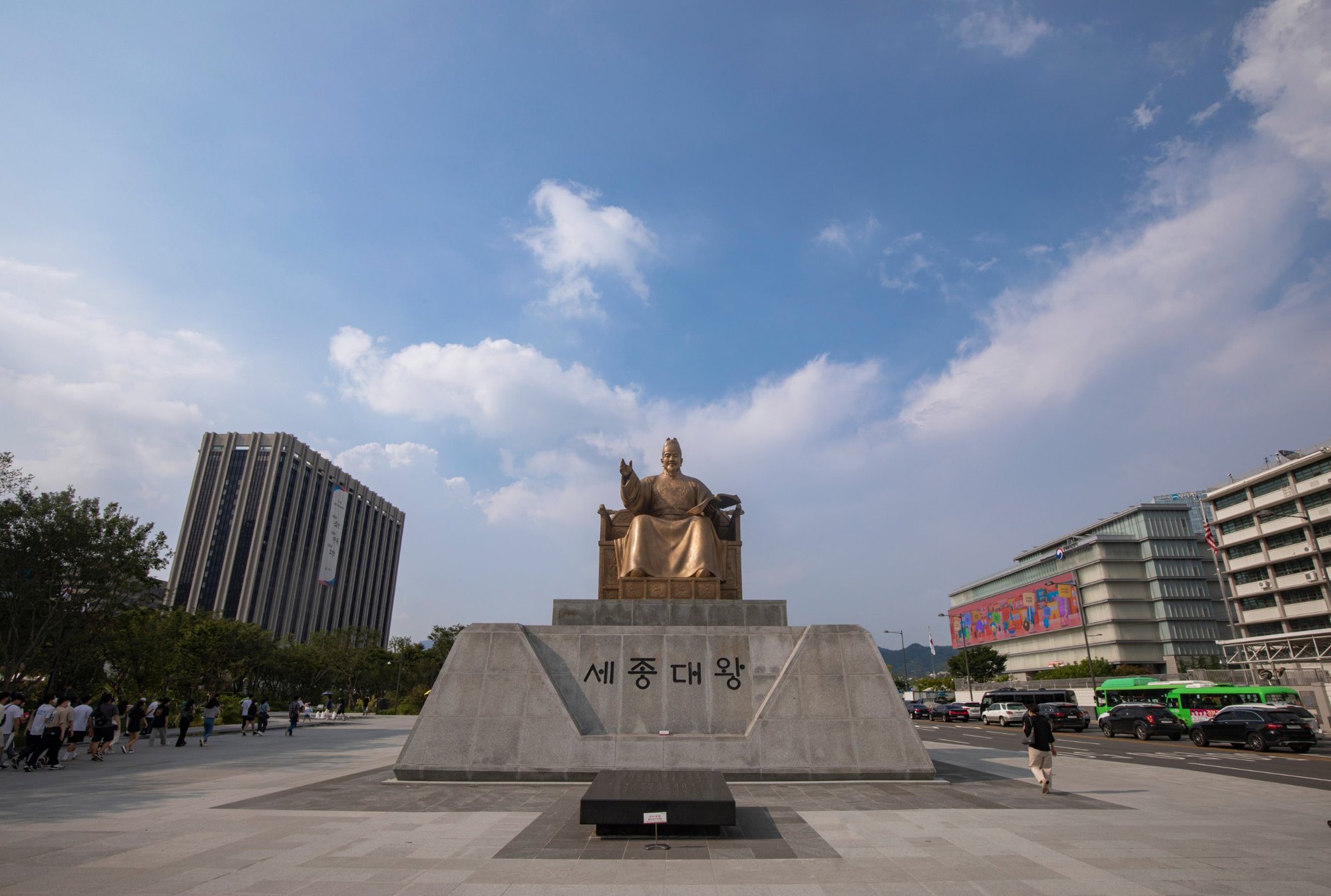 The gilded bronze statue of King Sejong seated on a throne in Gwanghwamun Square, with the gate and mountains behind.