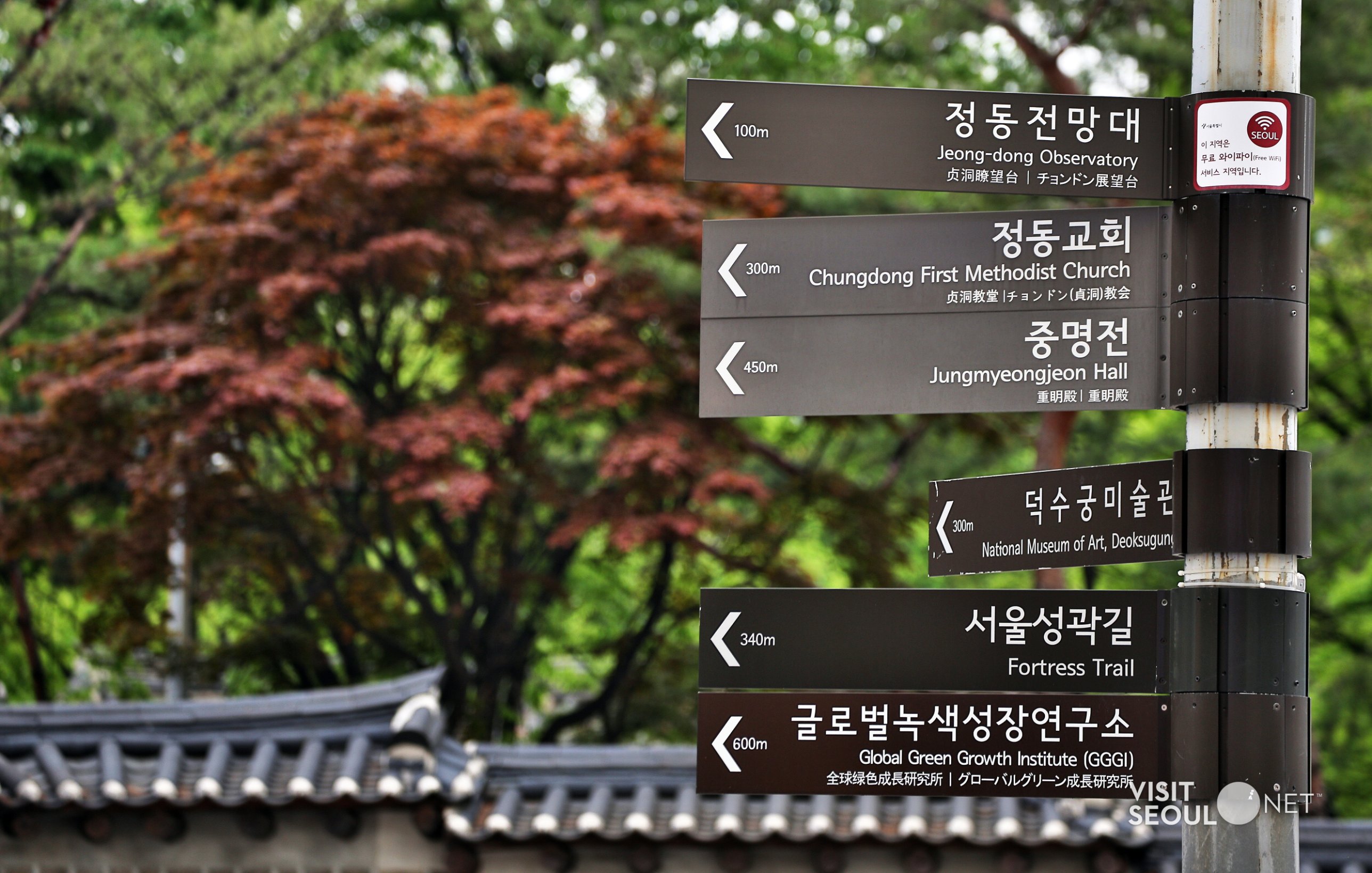 A cluster of brown directional signs on a pole in Jeong-dong, each with Hangeul on top and English below: Jeong-dong Observatory, Chungdong First Methodist Church, Jungmyeongjeon Hall, National Museum of Art Deoksugung, Fortress Trail.