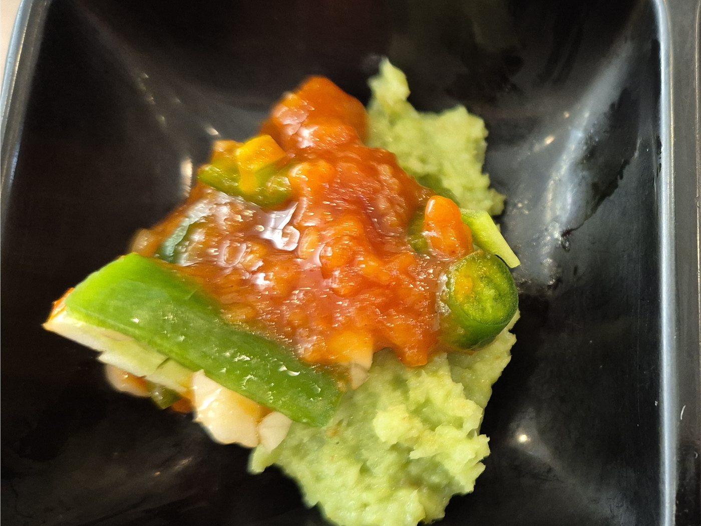 Pale green wasabi and red ssamjang in a black saucer, with sliced green chilli and garlic.