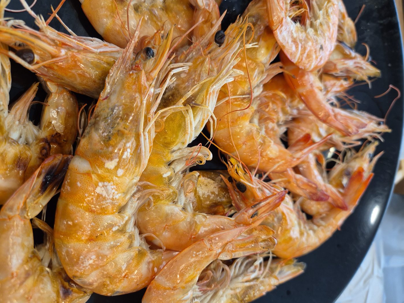 Salt-grilled shrimp piled high on a black plate, shells cooked orange.