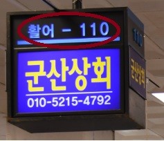 A shop sign. At the top the stall number '활어 - 110' (live fish – 110) is circled in red; below it, the shop name Gunsan Sanghoe and a phone number.