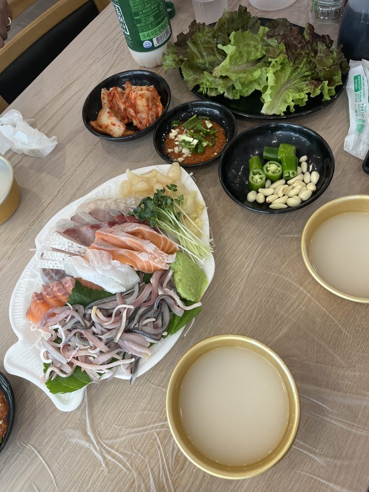 A table with the shad sashimi platter, lettuce, kimchi, chojang, chillies, garlic and two cups of makgeolli.